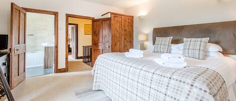 A bedroom with a large bed, wooden wardrobe, and a bathroom visible through an open door.