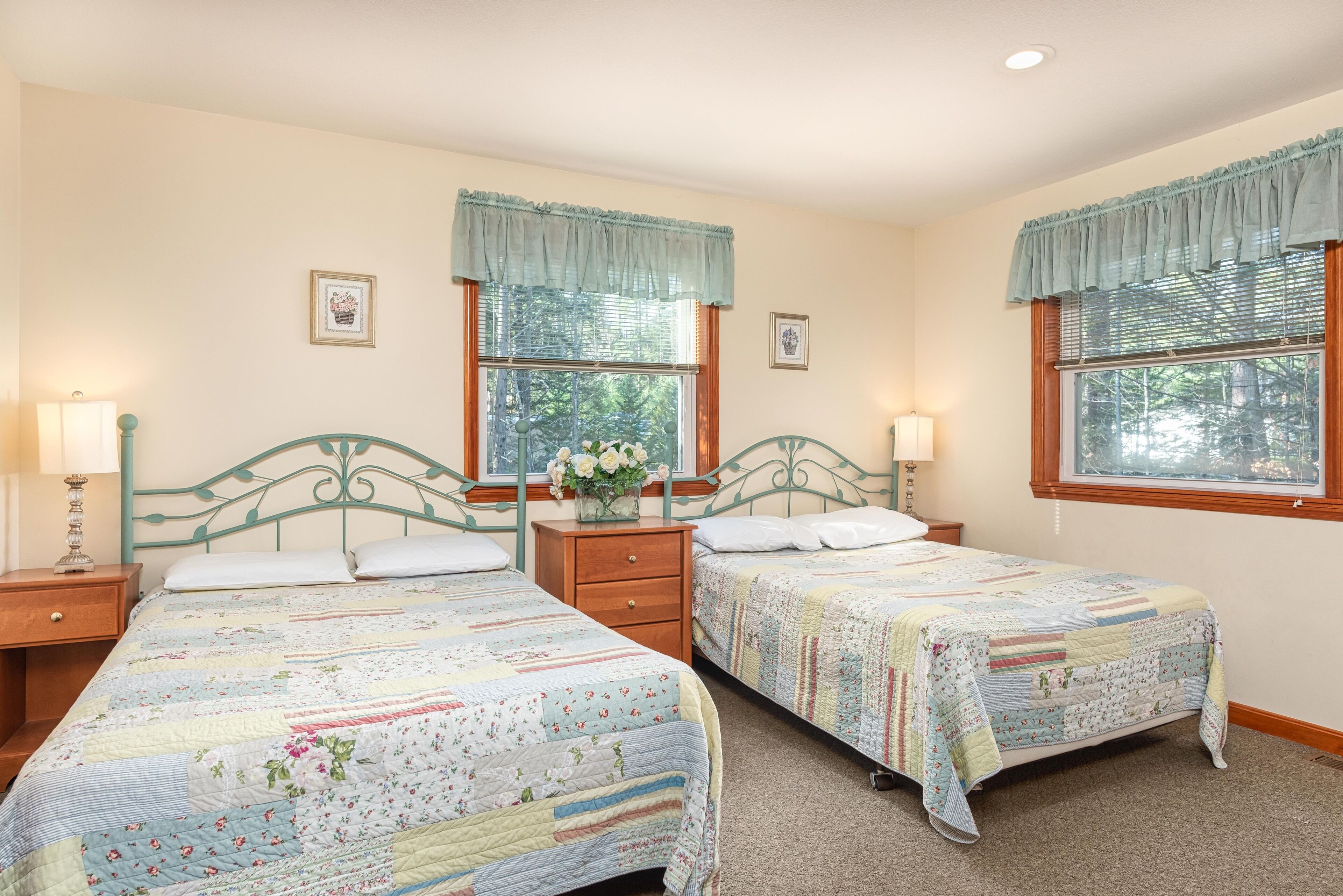 Une chambre à coucher avec deux lits, chacun recouvert d’une courtepointe à motifs floraux, dotés de têtes de lit en bois et de tables de chevet avec des lampes.