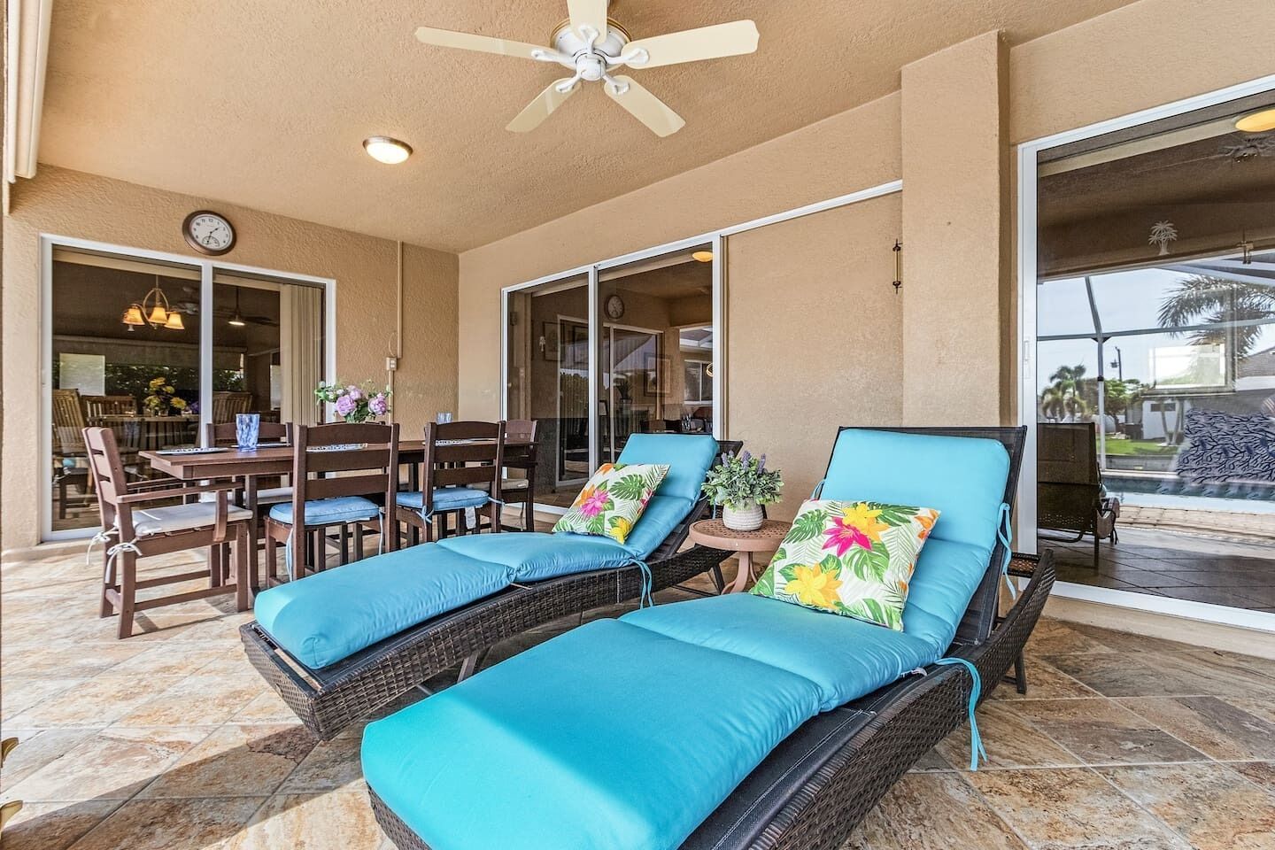 A covered outdoor seating area with wicker lounge chairs and a table, a ceiling fan, and a view of a pool.