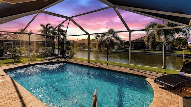 A swimming pool with a view of a body of water and palm trees, surrounded by a covered patio area.