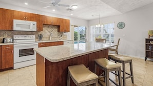 A modern kitchen with wooden cabinets, a central island with stools, a microwave, stove, and a ceiling fan.