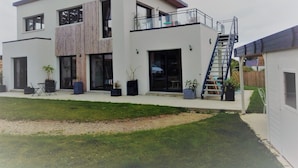 Une maison moderne à deux étages, dotée d’un balcon, d’un escalier et d’un petit jardin.