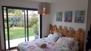 Une chambre avec un grand lit, une tête de lit en bois et une vue sur un jardin, accessible par une porte coulissante.