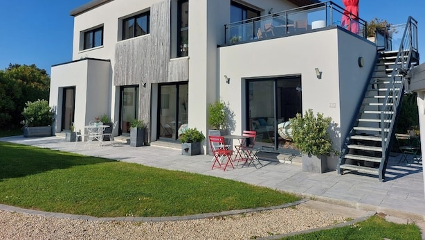 Une maison moderne à deux étages, dotée d’un balcon, de grandes fenêtres et d’un escalier menant à un niveau supérieur.