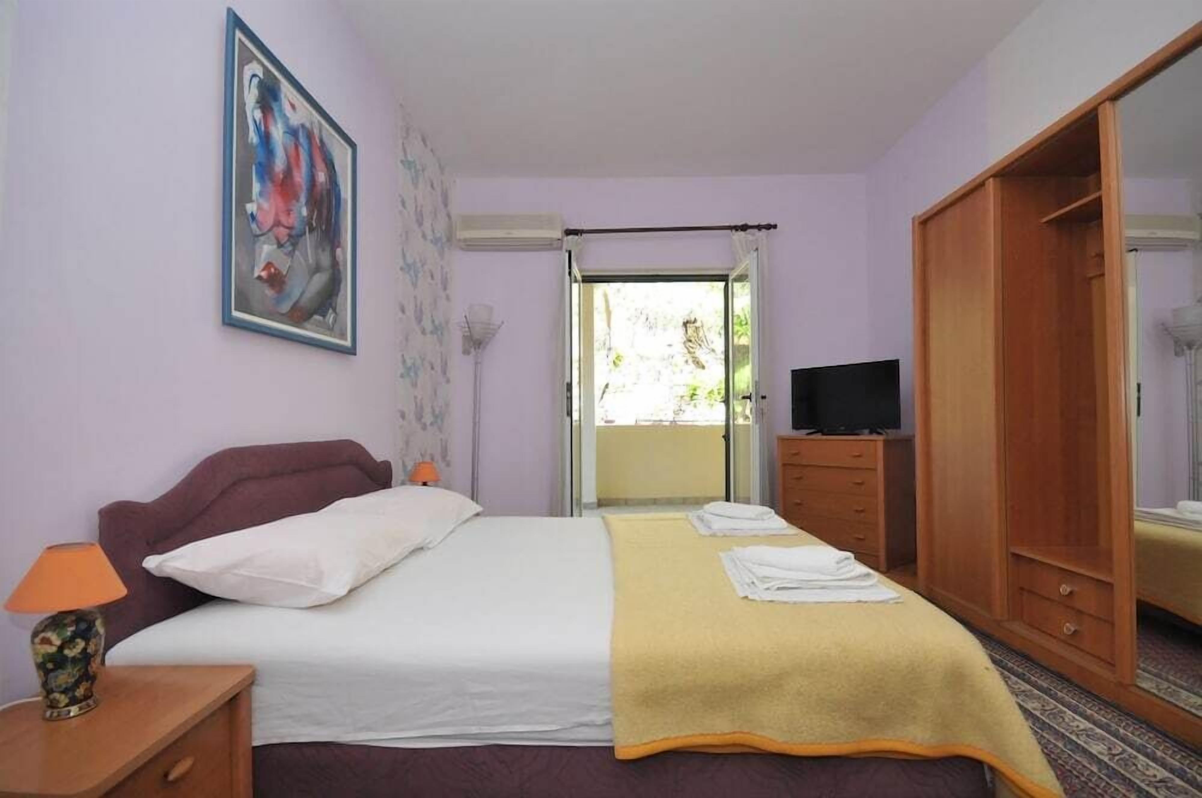 A hotel room with a bed, a TV, a wardrobe, and a painting on the wall.