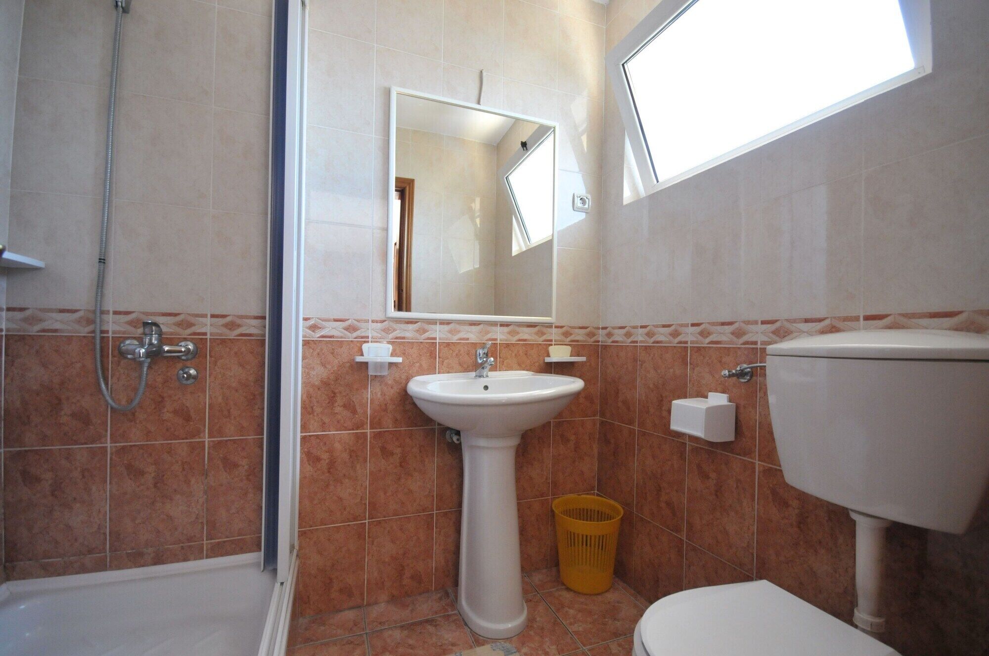 A bathroom with a shower, sink, toilet, and a mirror.