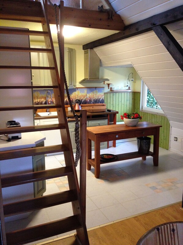 Een loft-stijl keuken met een houten trap, een eettafel en uitzicht op de woonkamer.