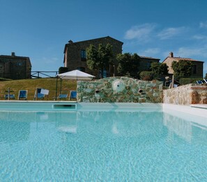 Ein klares, blaues Schwimmbecken mit Liegestühlen und einer Steinwand mit einem Rundfenster.