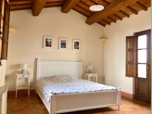 Ein Schlafzimmer mit einem weißen Bett, zwei Nachttischen, einer Holzbalkendecke und drei gerahmten Bildern an der Wand.