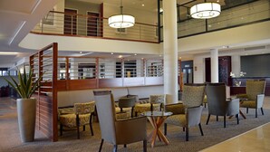 Eine großzügige Lobby mit hoher Decke, einer zentralen Sitzecke mit Stühlen und einem Tisch sowie einem dekorativen Holzparavet.