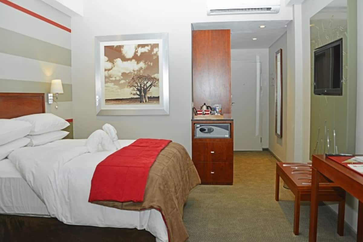 Ein Hotelzimmer mit Bett, Schreibtisch, Sessel, Fernseher und einem Gemälde an der Wand.