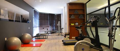 Un gimnasio con equipo de ejercicio, colchonetas rojas y suelo de madera.