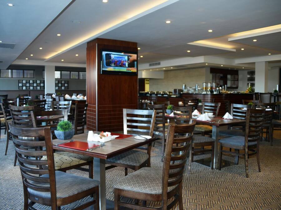 Un restaurante con varias mesas y sillas, un televisor montado en un pilar y una zona de bar al fondo.