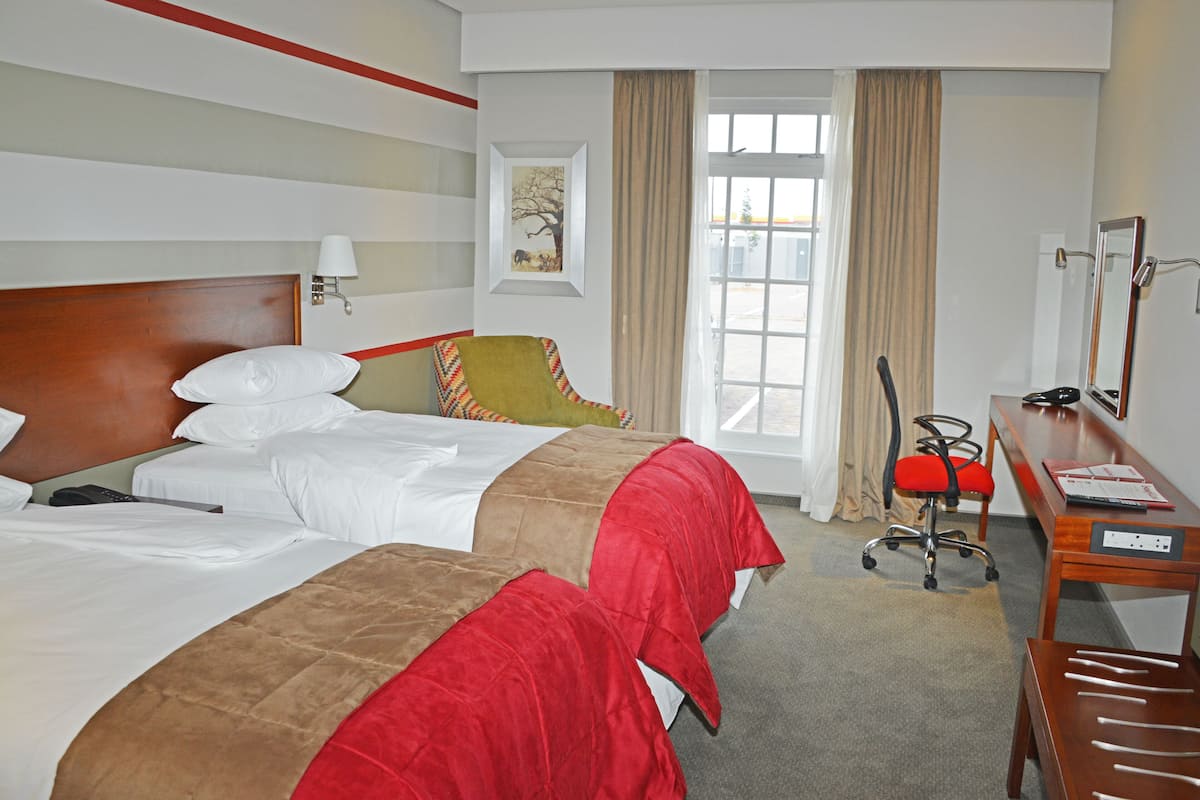 Ein Hotelzimmer mit zwei Betten, einem Schreibtisch, einem Sessel und einem Fenster mit Vorhängen.