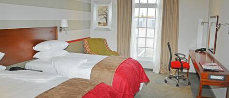 A hotel room with two beds, a desk, a chair, a lamp, and a window with curtains.