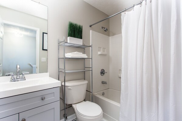 A modern bathroom with a white sink, toilet, and shower. There is a metal shelf unit with folded towels and a potted plant. - Decatur Gem w/King Bed, WiFi & Parking (Decatur)