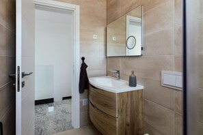 Un baño moderno con tocador de madera, lavamanos blanco y un espejo grande.