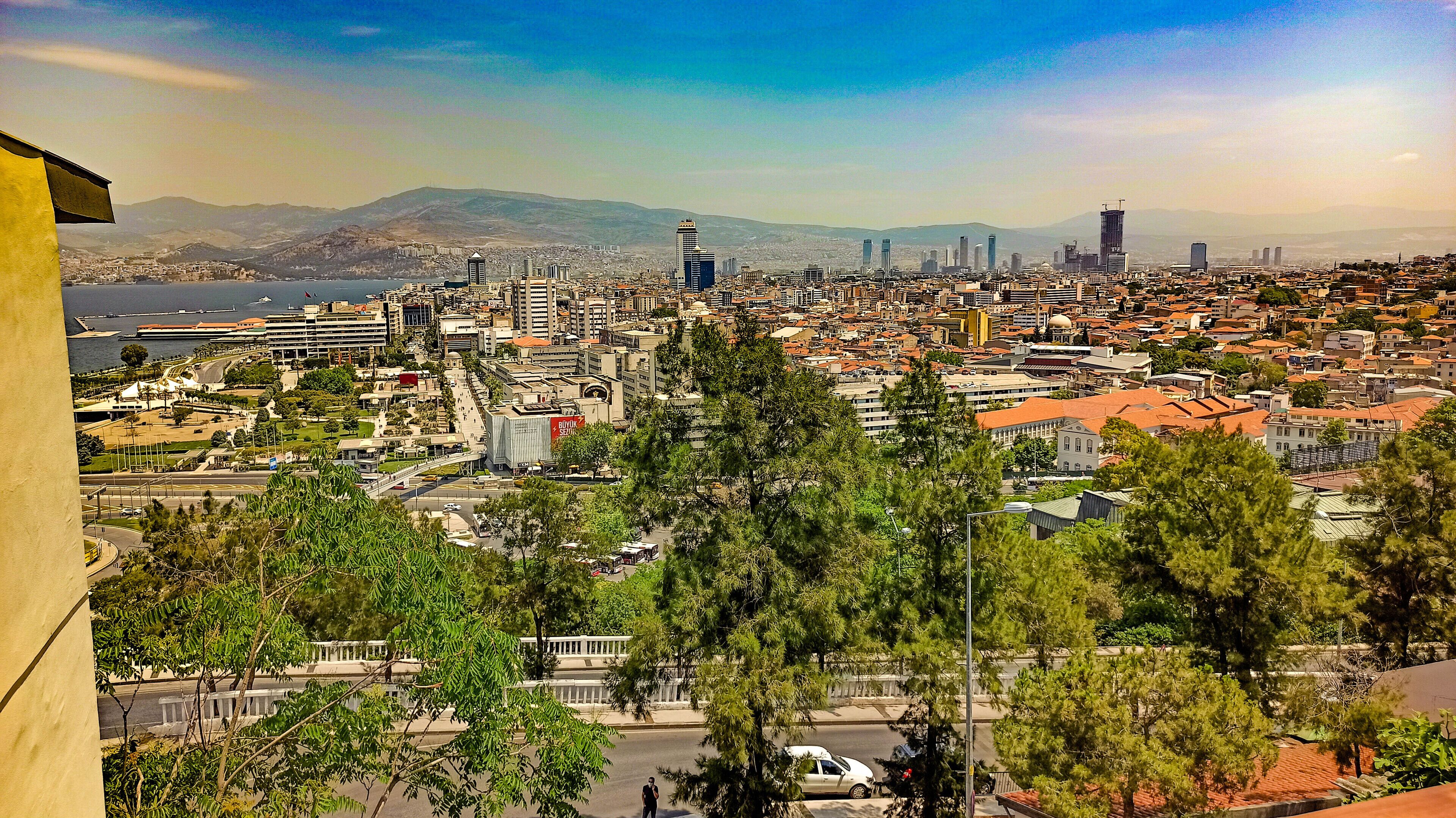 A cityscape with a mix of modern and traditional buildings, a prominent mosque, and a body of water in the distance.