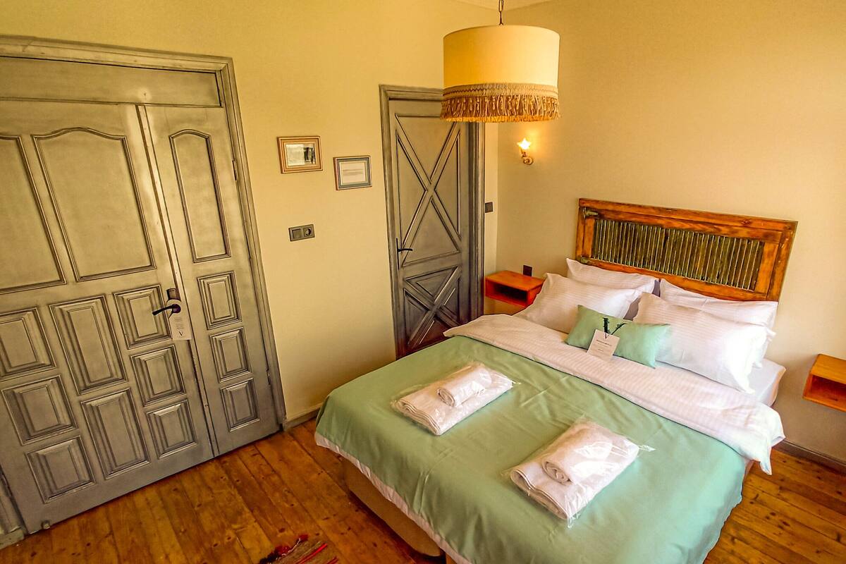 Una cama bien hecha con almohadas y toallas dobladas, un cabecero de madera y una lámpara colgante arriba.