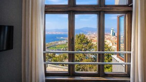 A room with a large window offering a cityscape view, including a body of water and distant mountains. - Variante Hotel (Izmir)