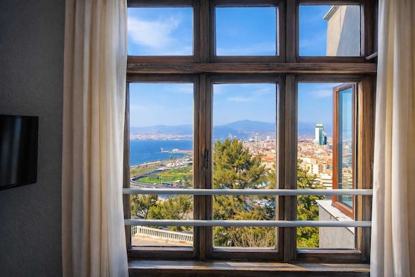 A room with a large window offering a cityscape view, including a body of water and distant mountains. - Variante Hotel (Izmir)