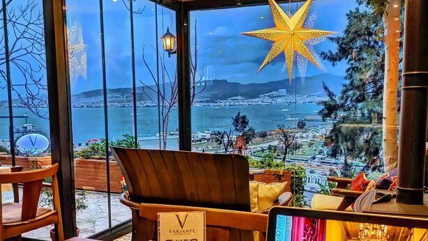 A cozy seating area with a view of the sea and cityscape, a QR menu sign, and a laptop on the table. - Variante Hotel (Izmir)