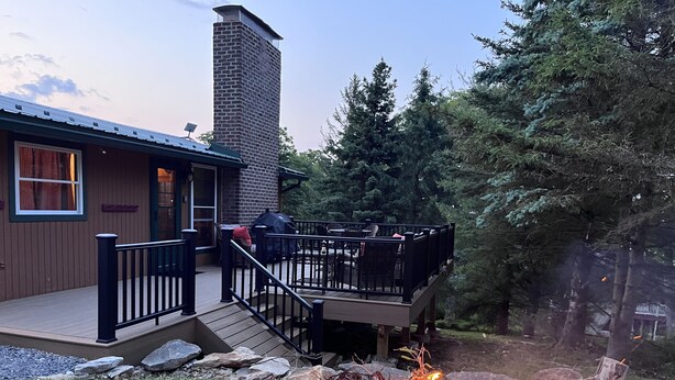 Une terrasse en bois avec des sièges d’extérieur, un foyer et une cheminée en pierre.