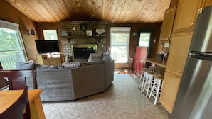 Un salon chaleureux avec une cheminée en pierre, un plafond en bois et un grand canapé d’angle gris.