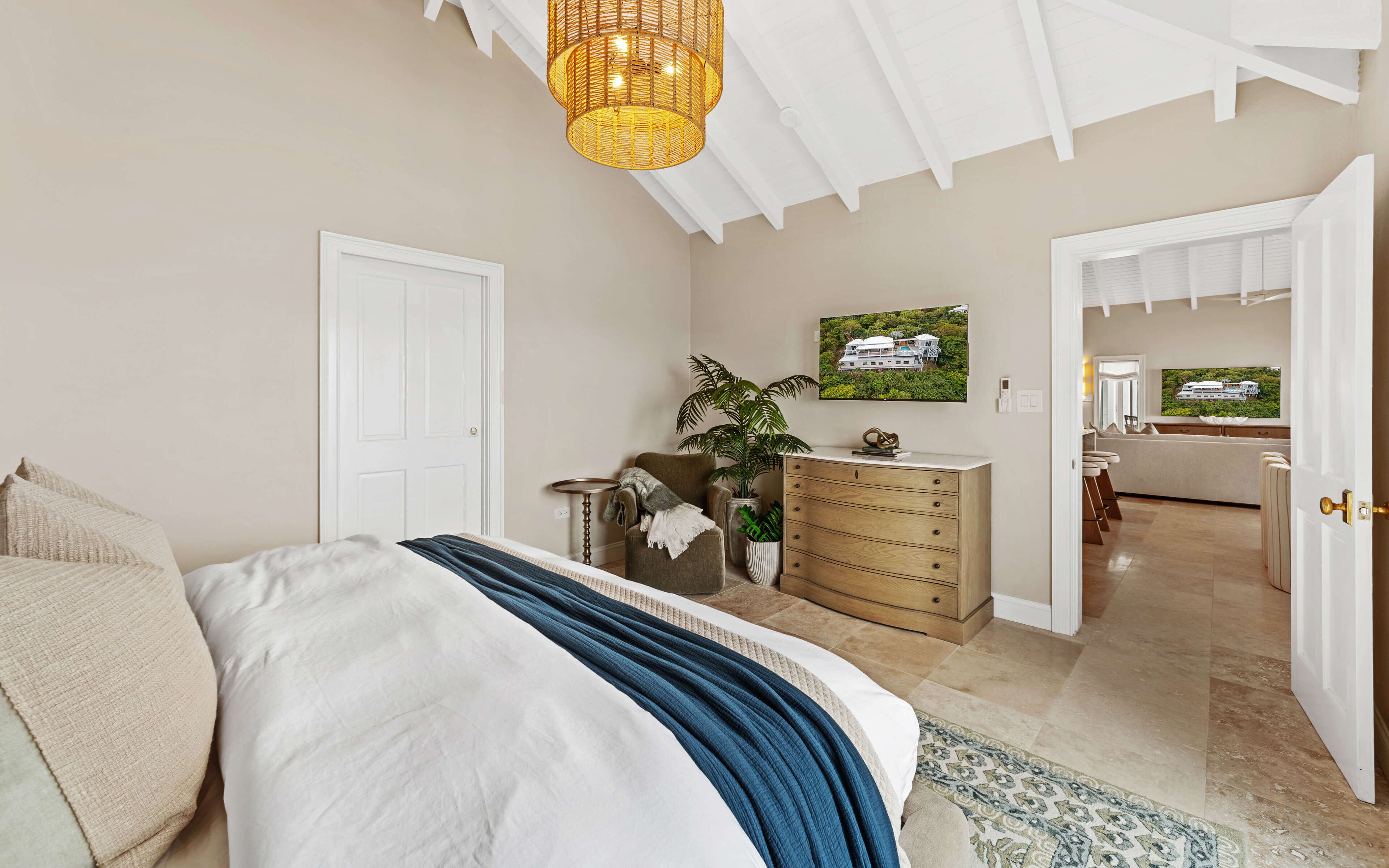 Quarto com cama, cômoda, planta e televisão na parede.