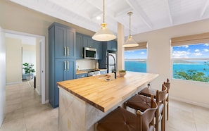 A modern kitchen with a wooden island, blue cabinets, and a view of the ocean.