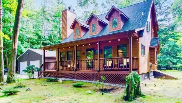 A large, two-story log cabin with a wrap-around porch and multiple windows. - Premier Cottage Getaway-Acorn Grove, Pentwater, MI (Pentwater)