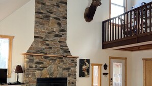 A spacious living room with a stone fireplace, leather sofas, a coffee table, and a mounted deer head. - Premier Cottage Getaway-Acorn Grove, Pentwater, MI (Pentwater)