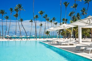 Ein Poolbereich mit Liegestühlen und Sonnenschirmen, Palmen und Blick aufs Meer.