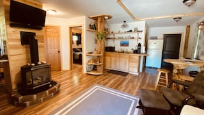 Una sala de estar acogedora con chimenea, pisos de madera, una zona de cocina con armarios de madera y un comedor con mesa y sillas.