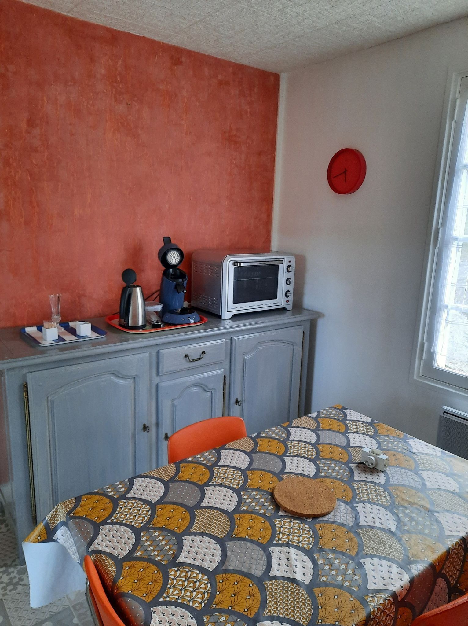 A small kitchen with a microwave, a kettle, and a clock on the wall.
