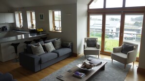 Ein modernes Wohnzimmer mit grauem Sofa, einem Couchtisch und Blick auf einen Garten durch große Fenster.