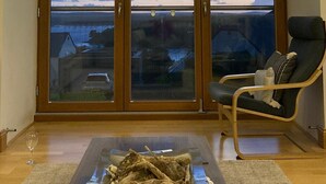 Ein Zimmer mit einem großen Erkerfenster, das auf eine reizvolle Landschaft blickt, einem Sessel und einem Tisch mit einem Glasbehälter.