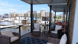 Een balkon met rieten meubilair, uitzicht op een jachthaven en gebouwen op de achtergrond.