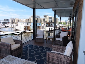 En balkon med fletningsmøbler, udsigt over en lystbådehavn og bygninger i baggrunden.