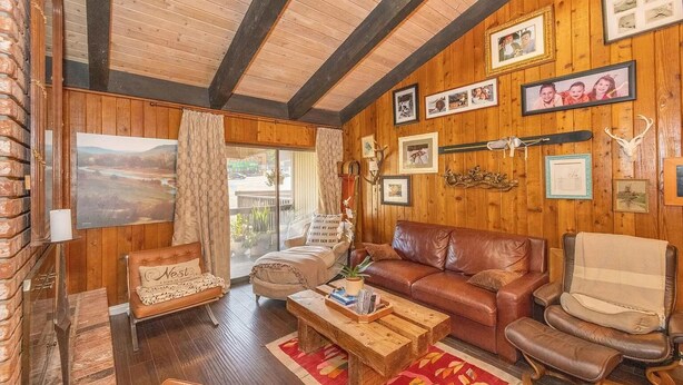 Una sala de estar acogedora con techo de madera, un sofá de cuero, una mesa de centro de madera y una chimenea.