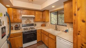 Una cocina con armarios de madera, estufa a gas, lavavajillas y ventana con vista a árboles.