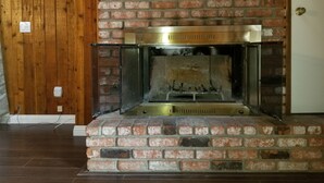 Una chimenea con una reja de metal, un marco de ladrillo y una pared de madera de fondo.