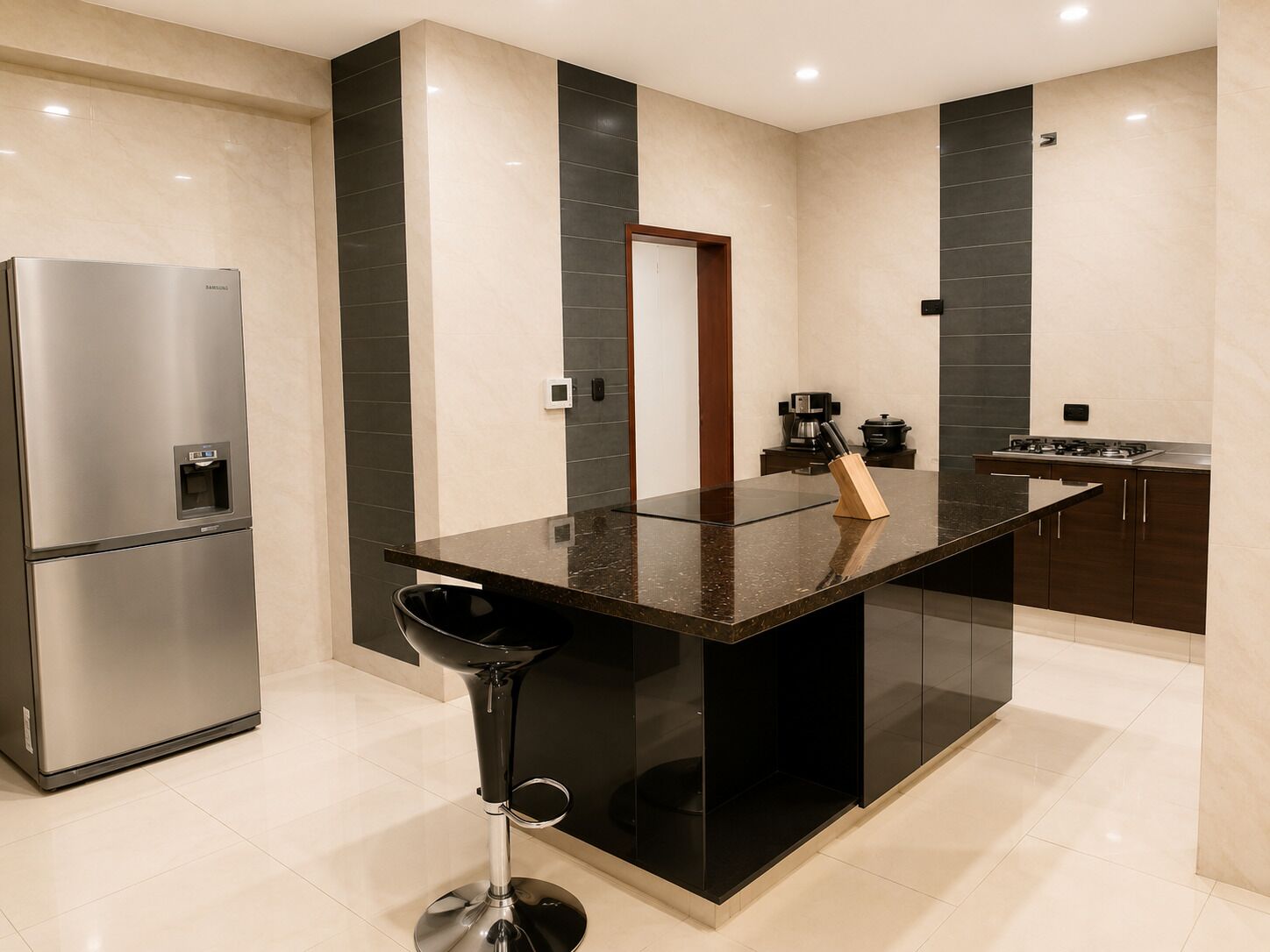 Una cocina moderna con un refrigerador de acero inoxidable, un taburete negro y una isla central con un bloque de cuchillos.