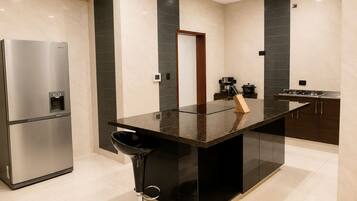 Una cocina moderna con un refrigerador de acero inoxidable, un taburete negro y una isla central con un bloque de cuchillos.