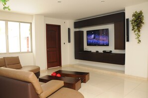 A modern living room with a flat-screen TV mounted on the wall, a dark wooden coffee table, and a brown sofa.