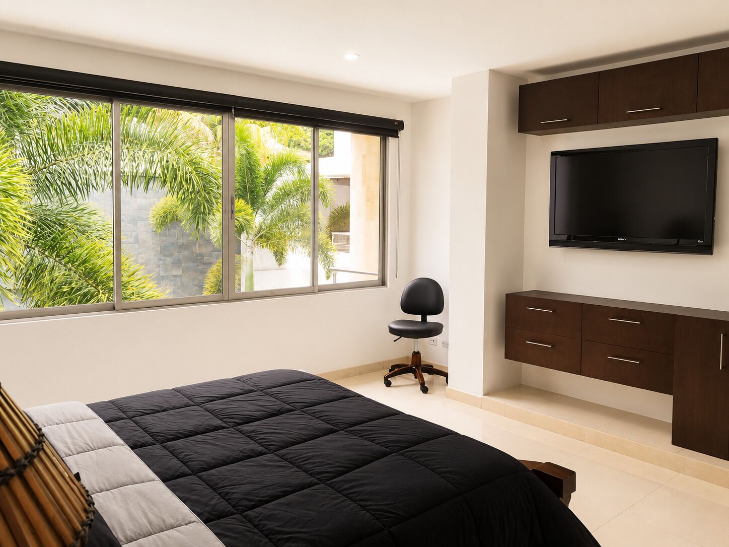 Een slaapkamer met een bed, een televisie en een raam met uitzicht op groen.