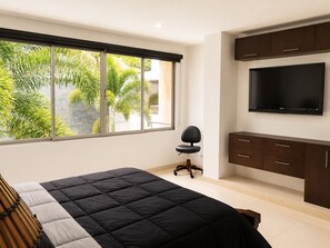 A bedroom with a bed, a TV, and a window with a view of greenery.
