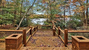 A wooden deck with a railing, surrounded by trees and a body of water.