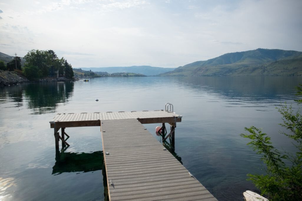 A wooden dock extending into calm water with a view of distant hills.