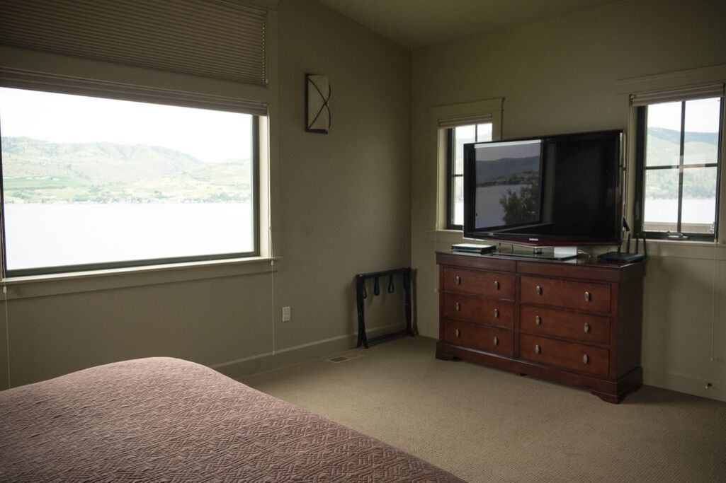 Ein Schlafzimmer mit Bett, Kommode, Fernseher und einem Fenster mit Blick auf Hügel.